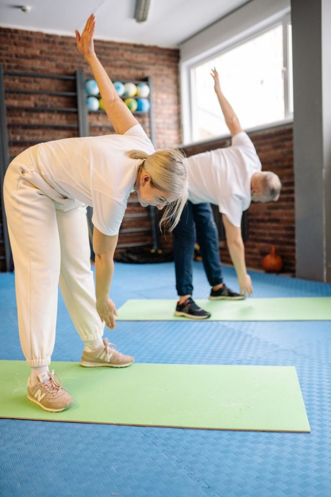 Senior adults stretch on mats in a fitness gym, promoting a healthy lifestyle.